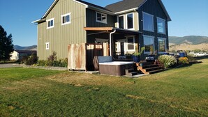 Une maison à deux étages dotée d’une grande terrasse, d’un espace salon extérieur et d’un jacuzzi.