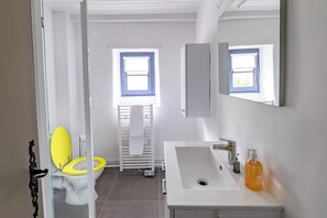 Une salle de bain avec un lavabo blanc, des toilettes jaunes, un porte-serviettes et une fenêtre avec des stores bleus.