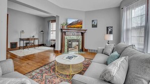 A living room with a fireplace, a sofa, a coffee table, and a TV. - Ideal & Exquisite Elmwood Village Victorian (Buffalo)