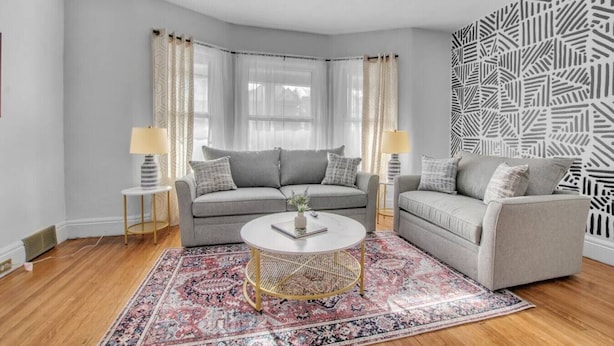 A modern living room with a grey sofa set, a round coffee table, and patterned curtains. - Large Charming Victorian Oasis in Elmwood Village (Buffalo)