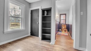 A hallway with a wooden floor, a bookshelf, and a door leading to another room. - Large Charming Victorian Oasis in Elmwood Village (Buffalo)