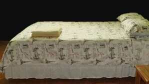 Una cama con una colcha estampada y almohadas, una mesita de noche de madera y un fondo oscuro.