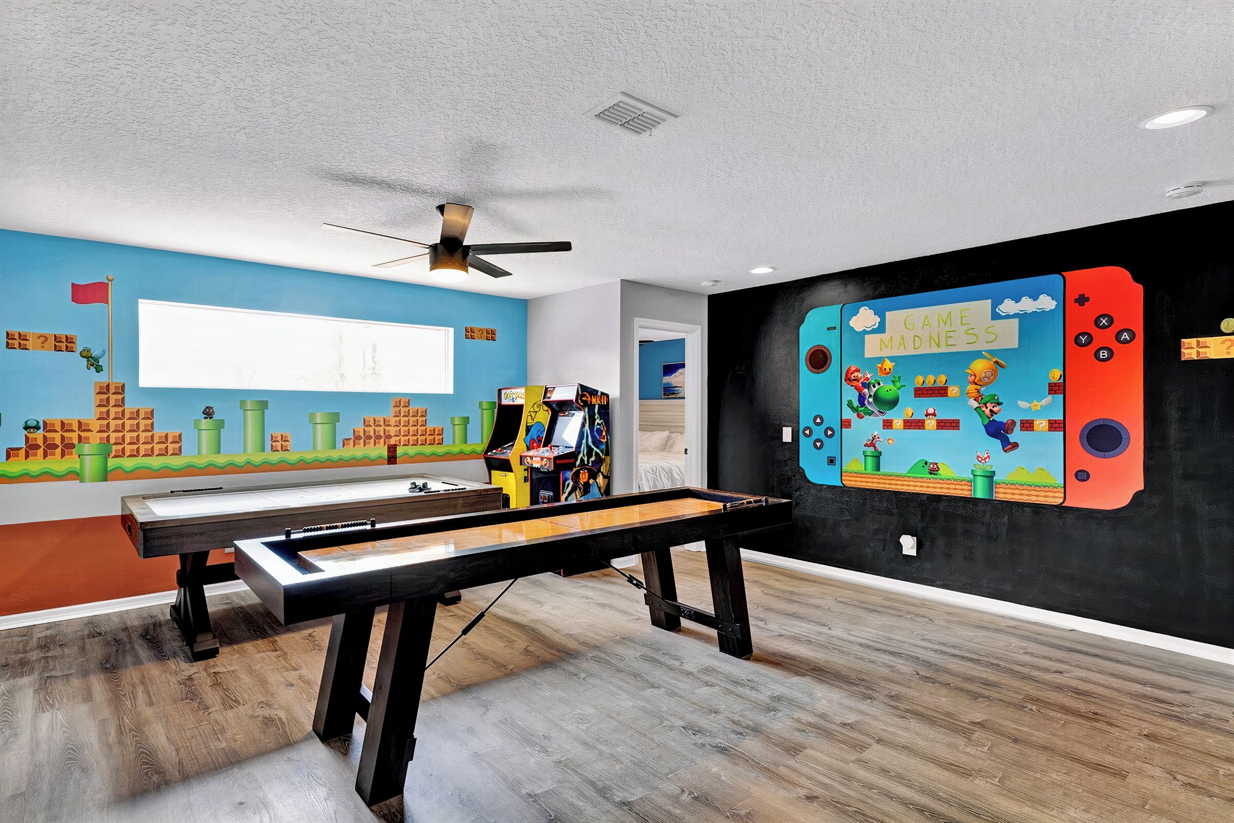 A room with a pool table, a ceiling fan, and colorful arcade game murals.
