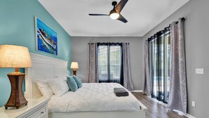 A bedroom with a bed, two bedside lamps, a ceiling fan, and a window with curtains.