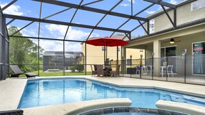 An indoor swimming pool with a glass ceiling, a hot tub, and outdoor seating with an umbrella.