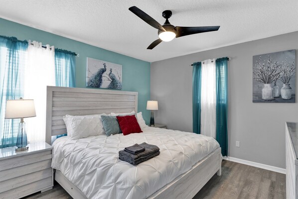 A bedroom with a bed, a ceiling fan, and a nightstand with a lamp.