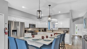 A modern kitchen with white cabinets, stainless steel appliances, and a central island with blue chairs.