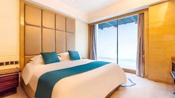 A modern hotel room with a large bed, a built-in headboard, a nightstand, and a large window offering a view.