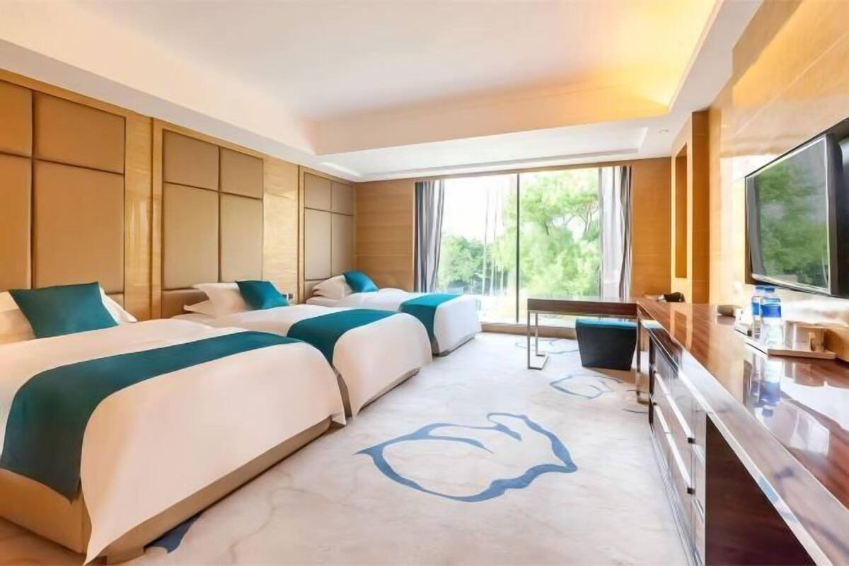 A hotel room with two beds, a desk, and a large window.