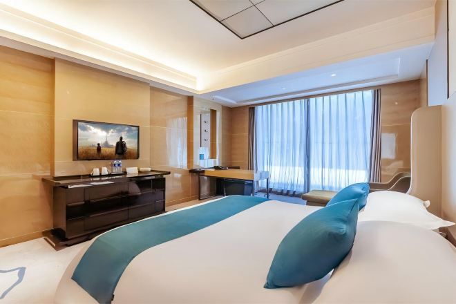 Habitación de hotel con cama, escritorio, silla, televisor y ventana con cortinas.