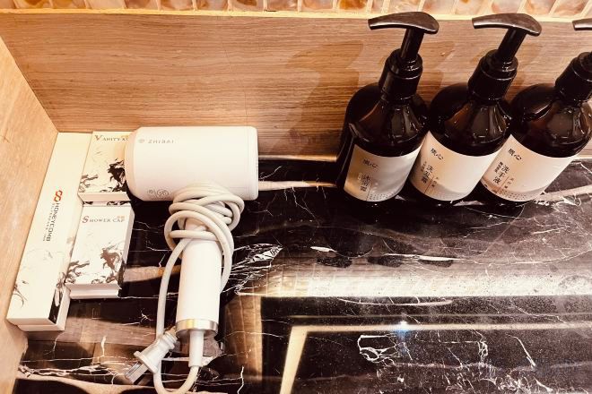 A bathroom with a marble countertop, a white power strip, and four bottles of shampoo.
