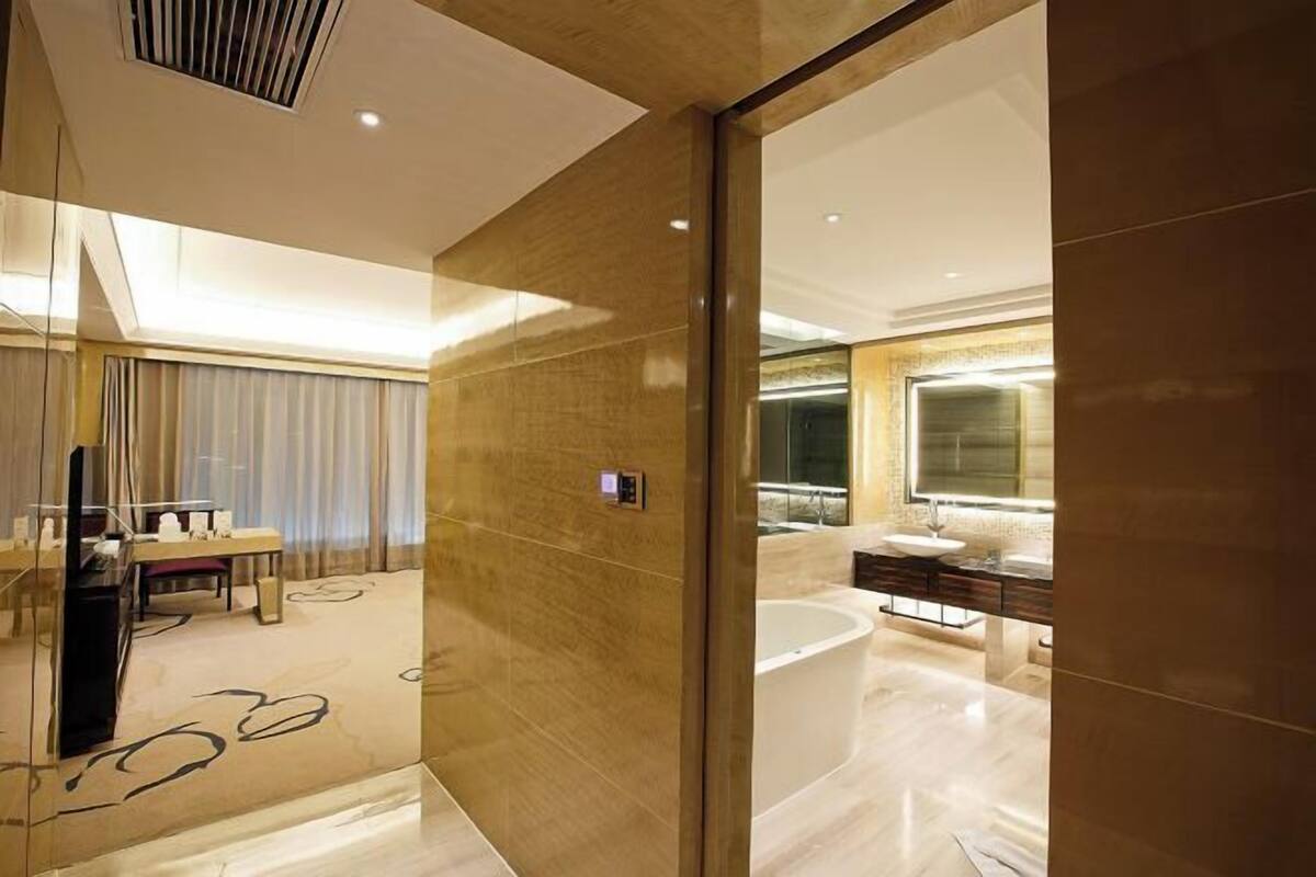 A modern hotel room with a large mirror, a bathtub, and a vanity with a sink.