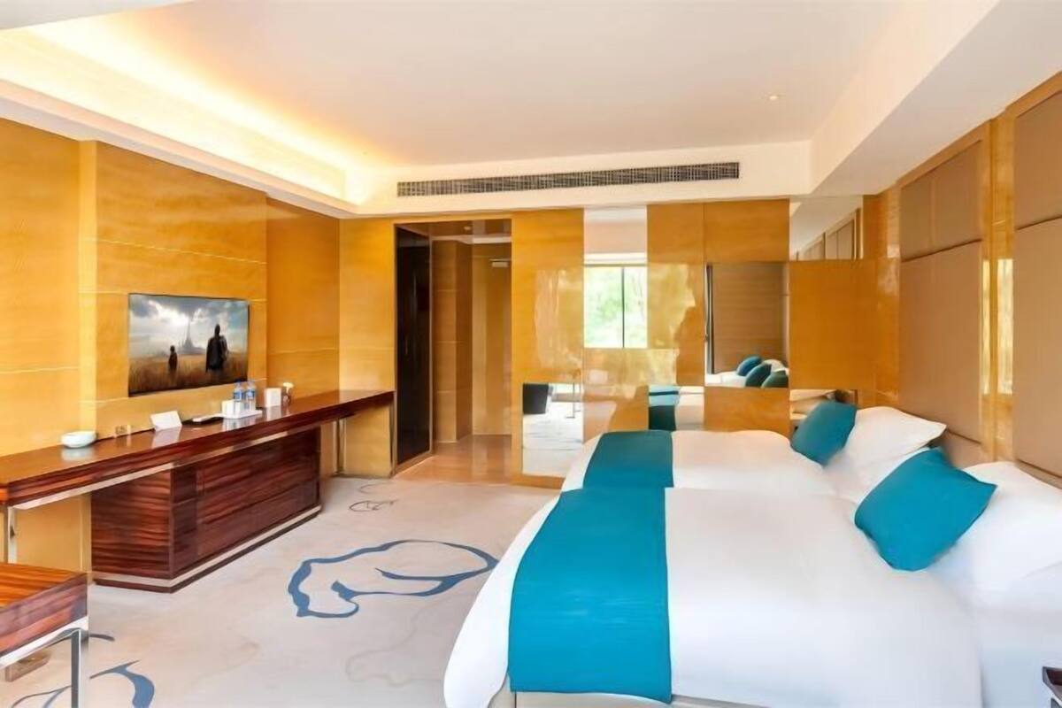 A modern hotel room with a large bed, a wooden console table, a flat-screen TV, and a large mirror.