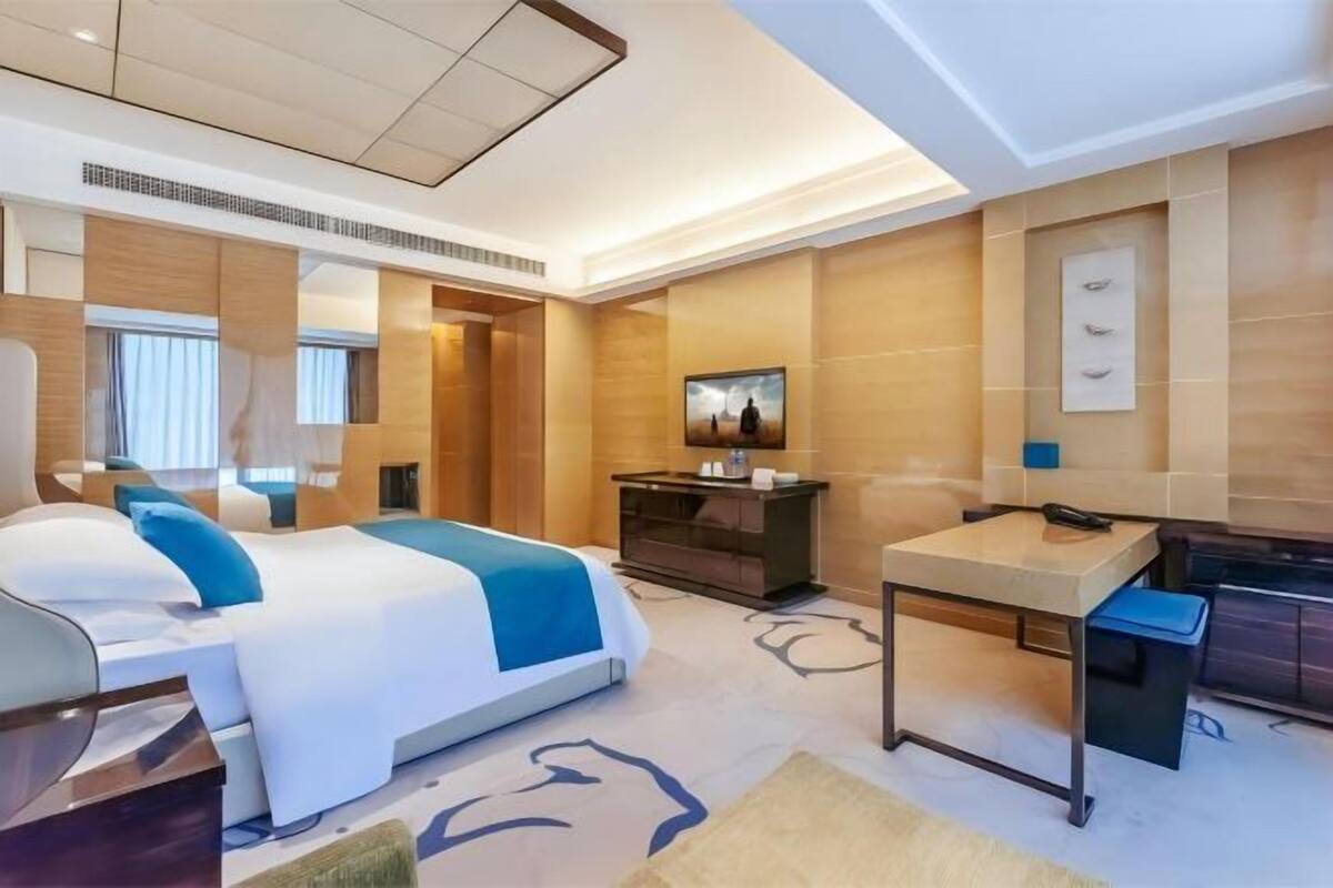 A modern hotel room with a bed, bedside table, and a desk with a chair.
