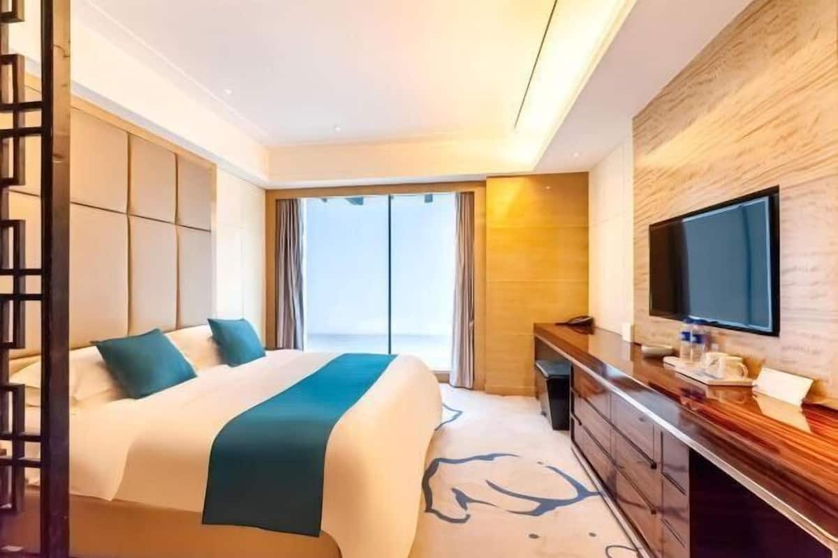 A hotel room with a large bed, a TV, a desk, and a view of the sea.