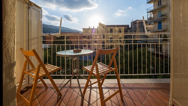 A balcony with two wooden chairs and a small round table, overlooking a residential area with buildings and a clear sky. - Amore&Psiche - De Vivo Realty Sorrento (Sorrento)