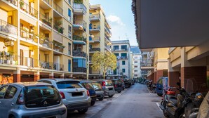 A narrow street lined with parked cars and motorcycles, multi-story buildings with balconies, and a clear sky. - Amore&Psiche - De Vivo Realty Sorrento (Sorrento)