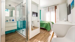 A modern bedroom with a glass shower enclosure, a green bed, and a white desk. - Amore&Psiche - De Vivo Realty Sorrento (Sorrento)