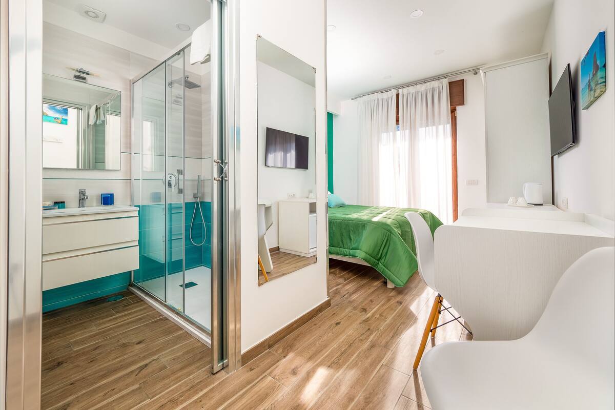 Un dormitorio moderno con cabina de ducha de vidrio, cama verde y escritorio blanco.