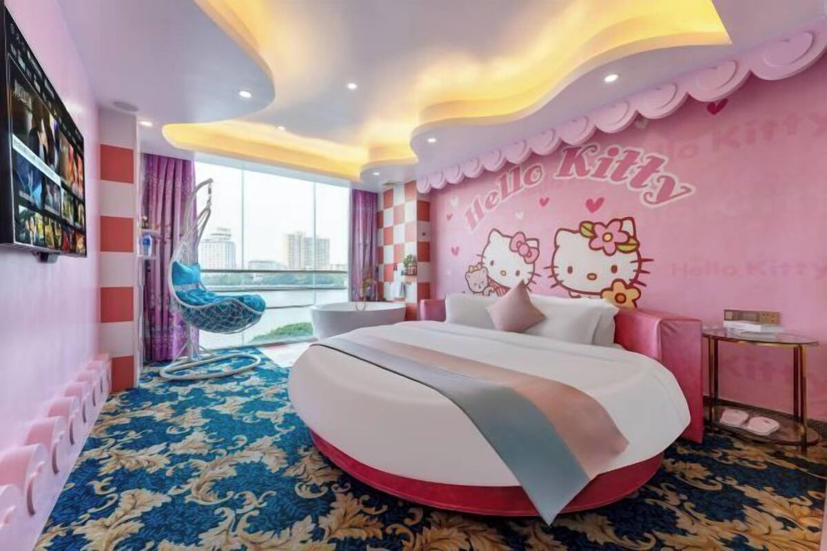 A pink-themed room with a Hello Kitty mural, a bed, a chair, and a view of the city.