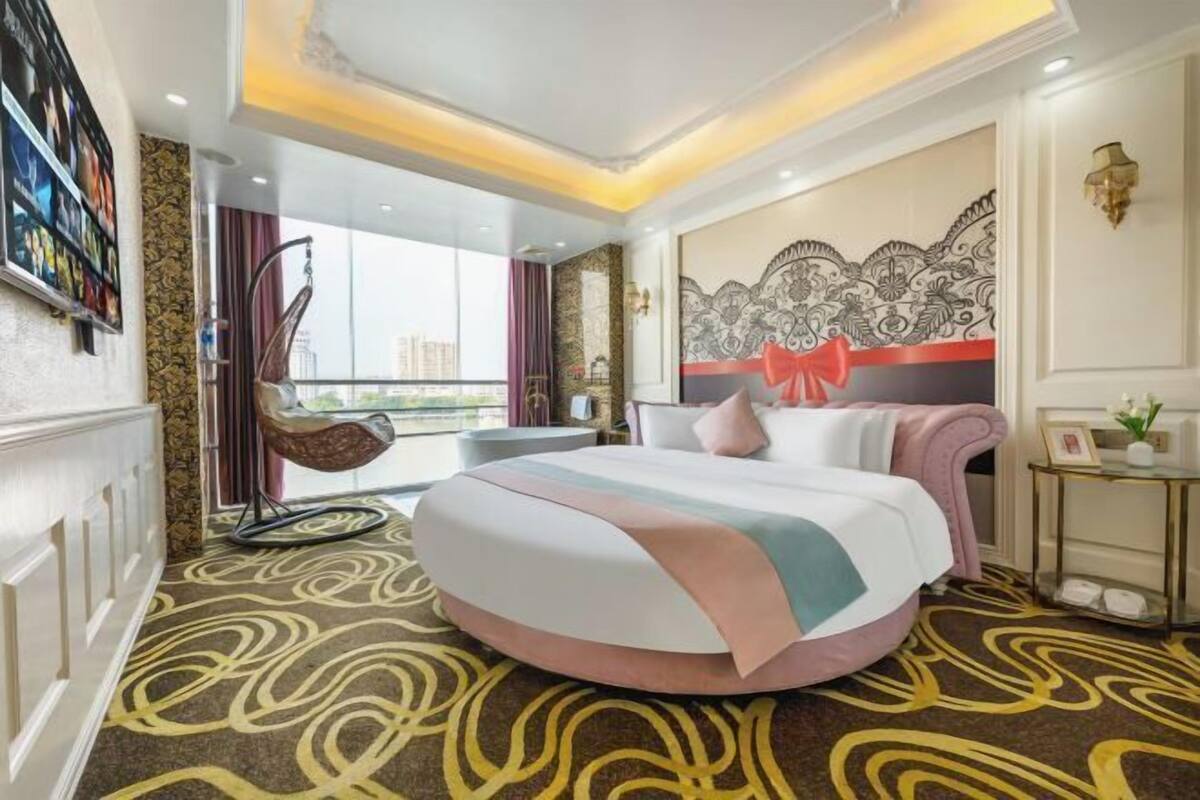 A hotel room with a bed, a chair, a wall with a decorative pattern, and a view of buildings outside.