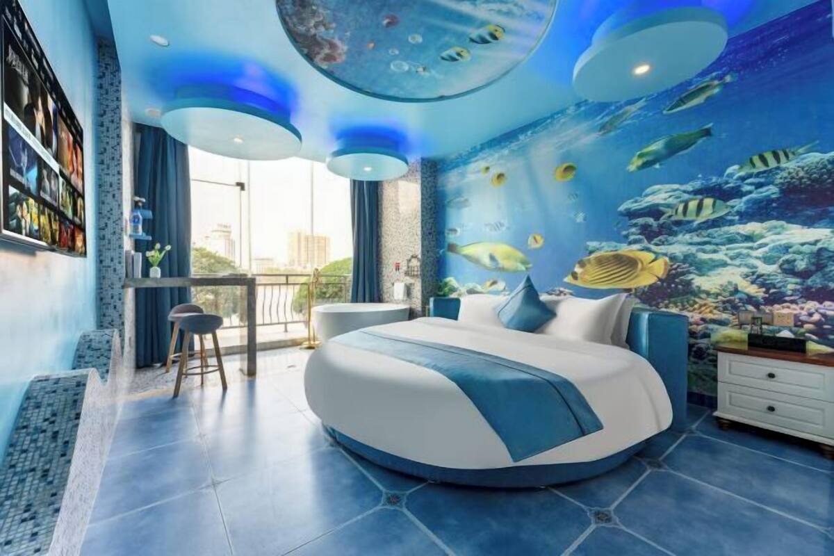 A bedroom with a bed, a desk, and a chair, featuring an underwater mural on the wall.