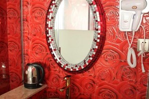 A bathroom with a red rose-patterned wall, a round mirror with a mosaic frame, a hairdryer, and a kettle on the counter. - Aiqing Apartment Chain Hotel (Kaiping)
