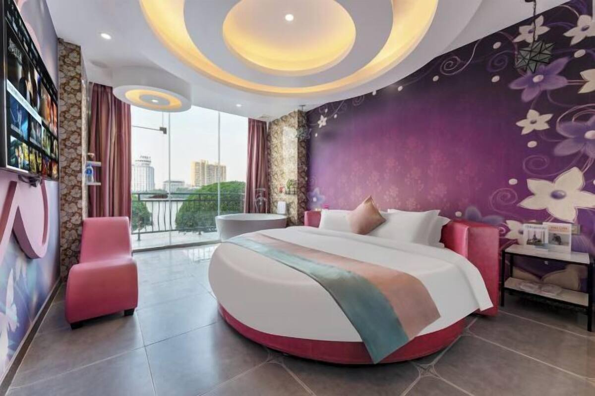 A modern bedroom with a curved bed, a city view, and a decorative wall.