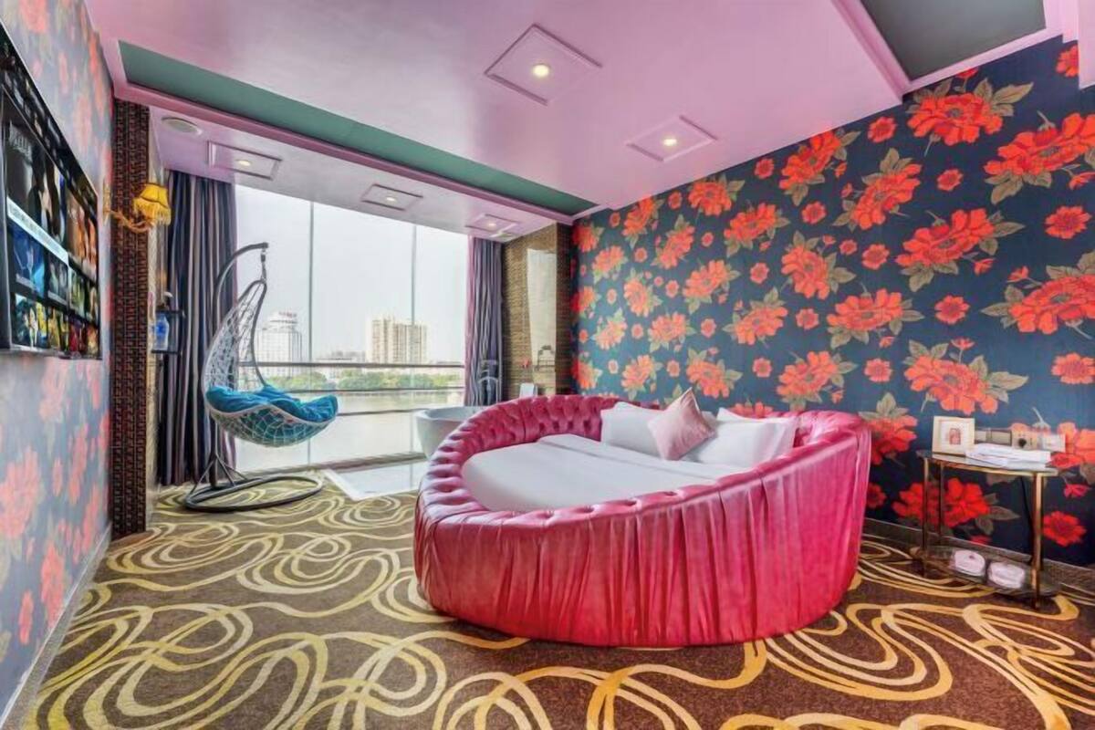 A room with a circular bed, a hanging chair, a bookshelf, and a view of the city.