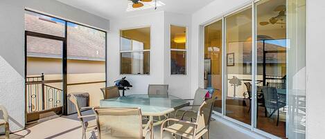 A spacious balcony with a glass table and chairs, a ceiling fan, and a view of the building's interior.