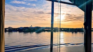Vista attraverso una finestra su un fiume, edifici sulla riva opposta, un ponte e un tramonto.