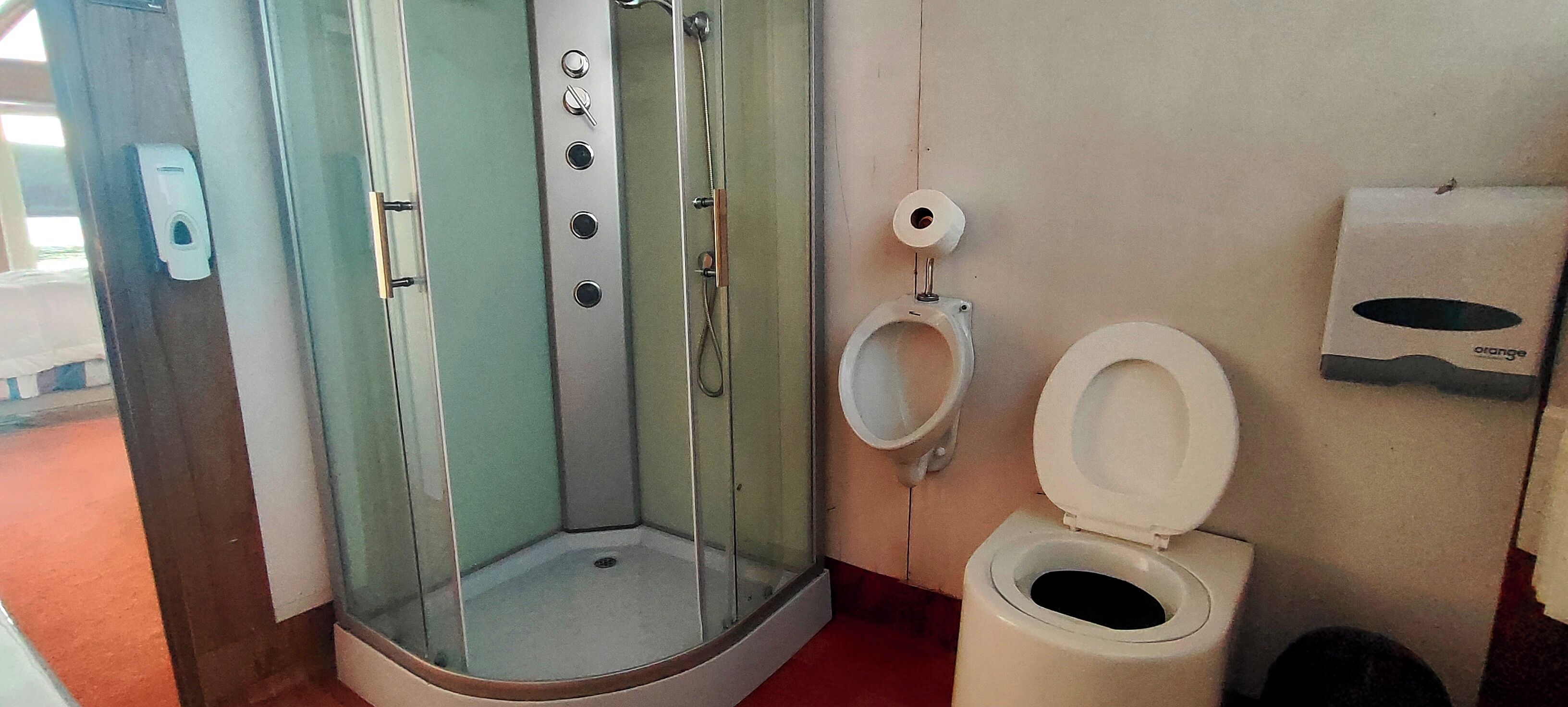 Un baño con ducha acristalada, inodoro y dispensador de toallas de papel.