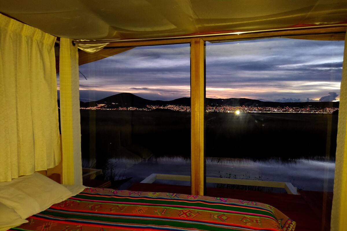 Una habitación con un amplio ventanal que da a una vista urbana al anochecer.