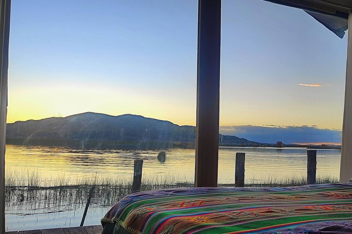 Un dormitorio con una cama, vista a un lago y montañas a lo lejos.