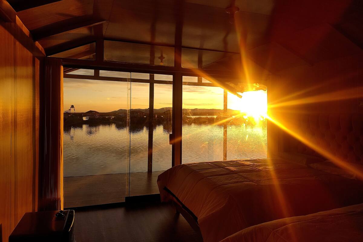 Una habitación con un ventanal grande que da a un cuerpo de agua y un atardecer.