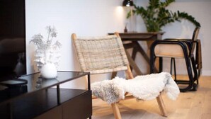 Ein modernes Wohnzimmer mit einem schwarzen TV-Schrank, einem Korbstuhl, einem weißen, flauschigen Hocker und einem Esstisch mit Stühlen.