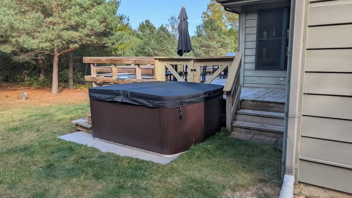 Een bubbelbad in een achtertuin met een houten terras en een huis op de achtergrond.