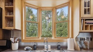 Una cocina con un lavamanos doble, armarios de madera y una ventana con vistas a árboles.