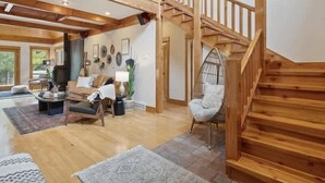 Amplia sala de estar con techo alto, escalera de madera y una silla colgante.