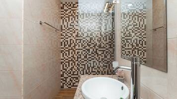 A bathroom with a tiled shower, a sink with a faucet, and a mirror.