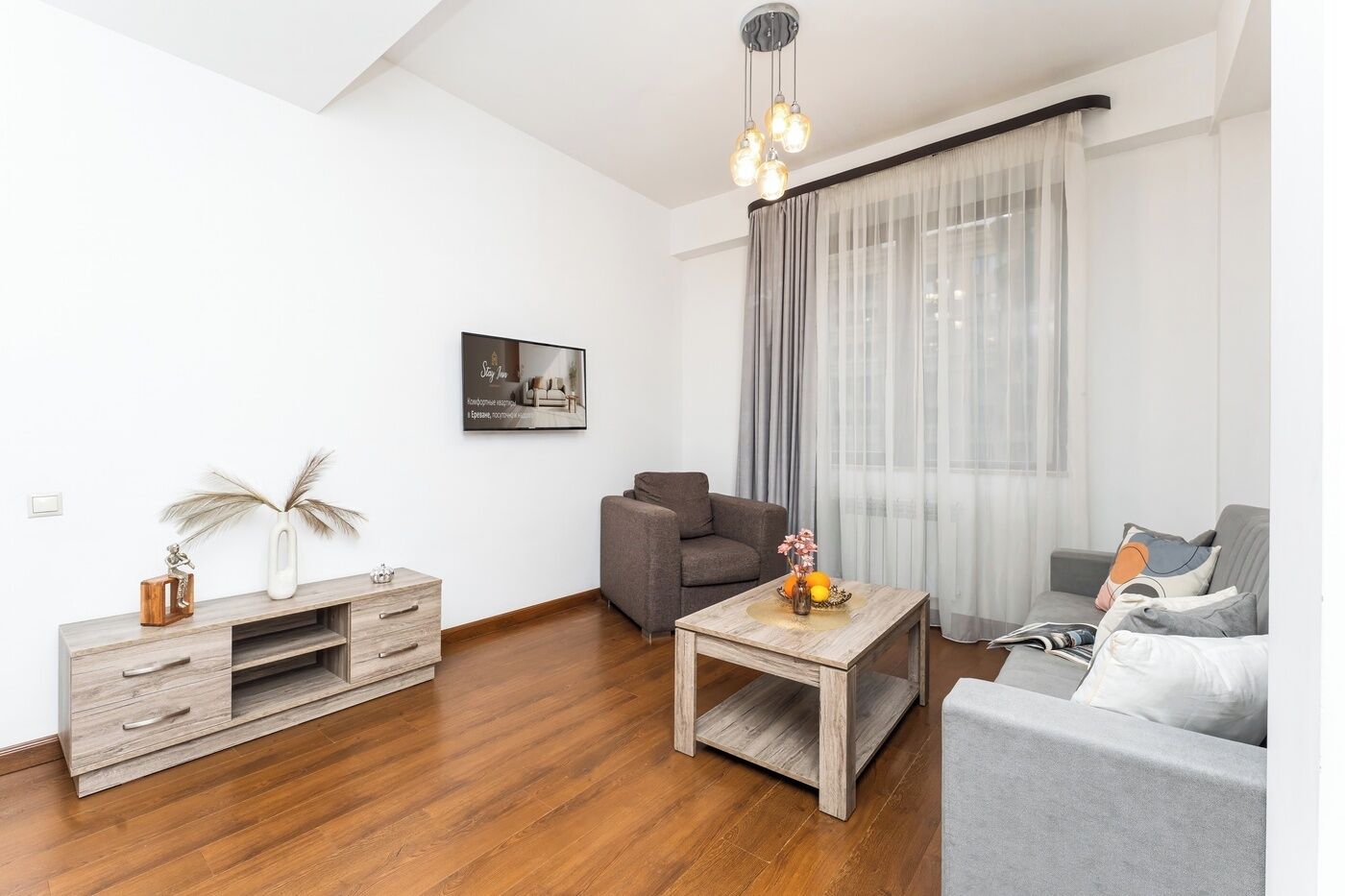 A modern living room with a sofa, a coffee table, a TV stand, and a large window with curtains.