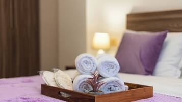 A wooden tray with rolled towels and a potted plant on a bed with a purple blanket.