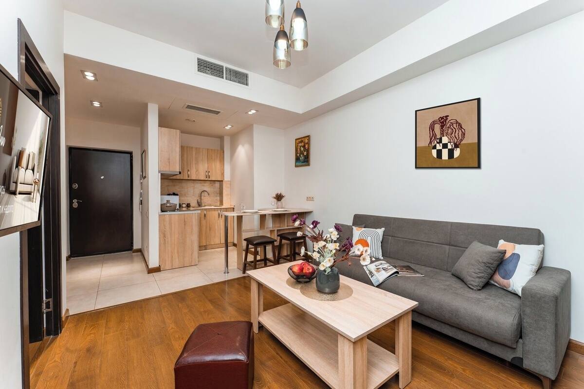 A modern living room with a grey sofa, wooden coffee table, and a dining area with a kitchen in the background.