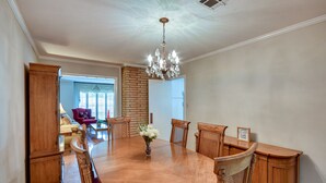 Uma sala de jantar com uma grande mesa de madeira, seis cadeiras, um candelabro e uma parede de destaque em tijolo.