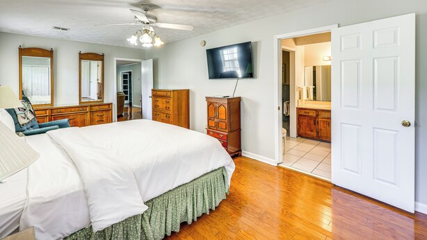 Quarto com cama, cómoda de madeira e televisão na parede.