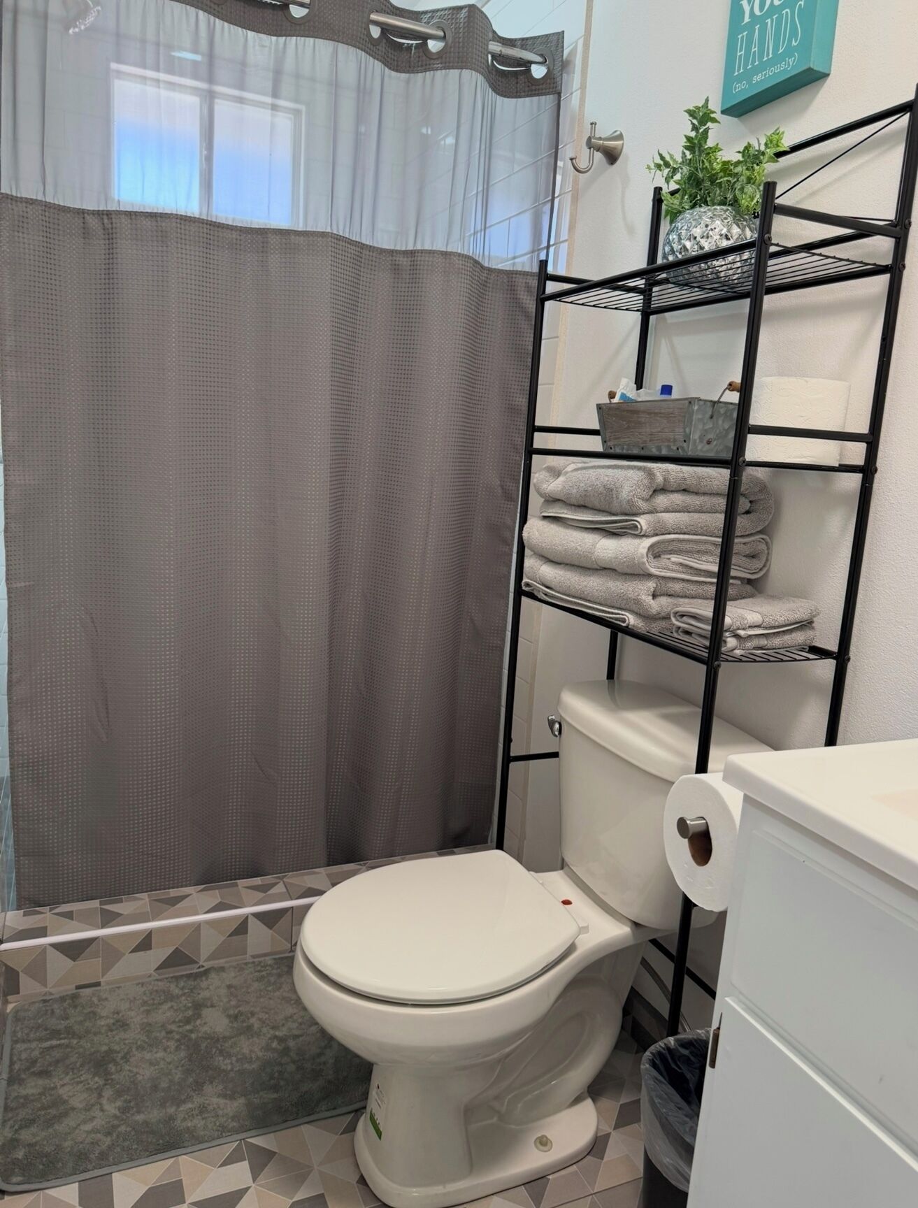 A bathroom with a toilet, a shower curtain, a towel rack with folded towels, and a toilet paper holder.