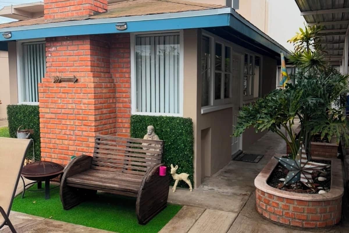 A house with a brick chimney, a blue roof, and a garden with a bench and a statue.