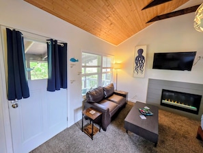 A living room with a fireplace, a sofa, a coffee table, and a television. - Cozy Cottage • Fire Pit • Walk to Bay (Lincoln City)