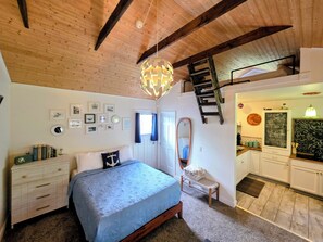 A bedroom with a bed, dresser, and a mirror. There is a staircase leading to an upper level. - Cozy Cottage • Fire Pit • Walk to Bay (Lincoln City)