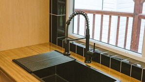 Eine Küche mit einem schwarzen Spülbecken, Holzschränken und einem Fenster mit Blick auf eine Holzterrasse.